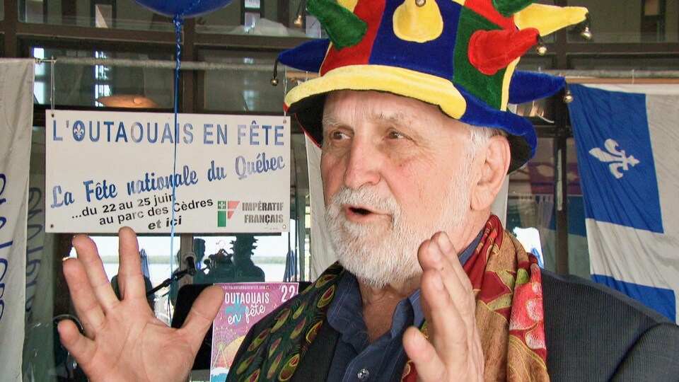 Un homme à la barbe blanche coiffé d'un chapeau multicolore s'exprime en entrevue.