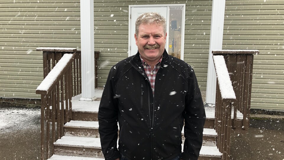 Un homme debout devant une maison. Il neige. 