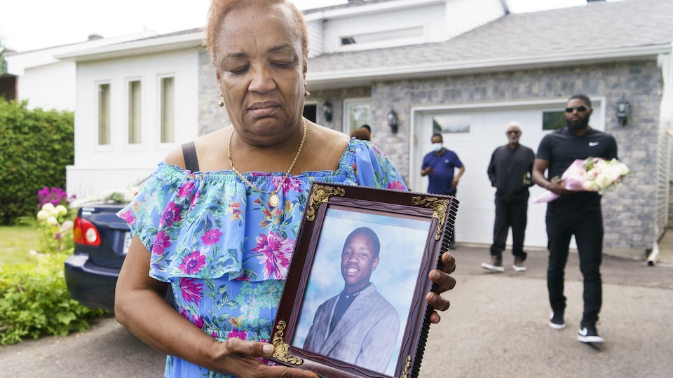 La mère tient un cadre dans lequel se trouve une photo de son fils.