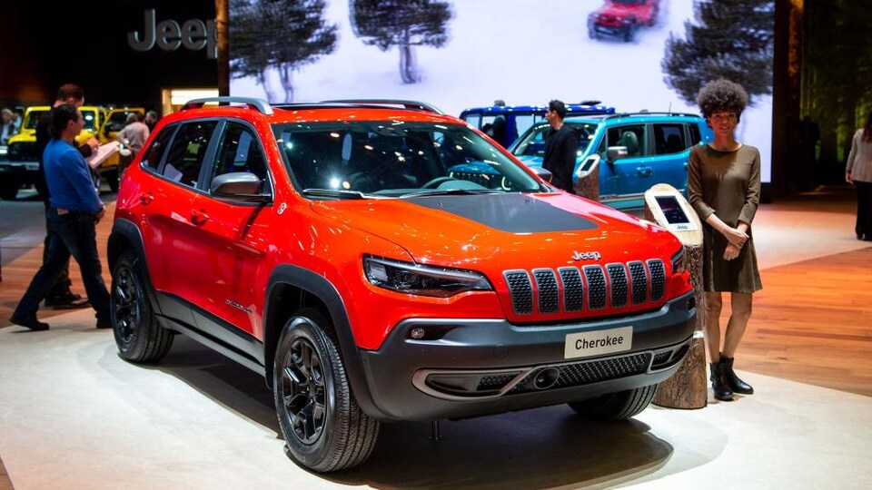 Un véhicule Jeep Cherokee exposé dans un salon de l'auto. Une femme se tient près du véhicule.
