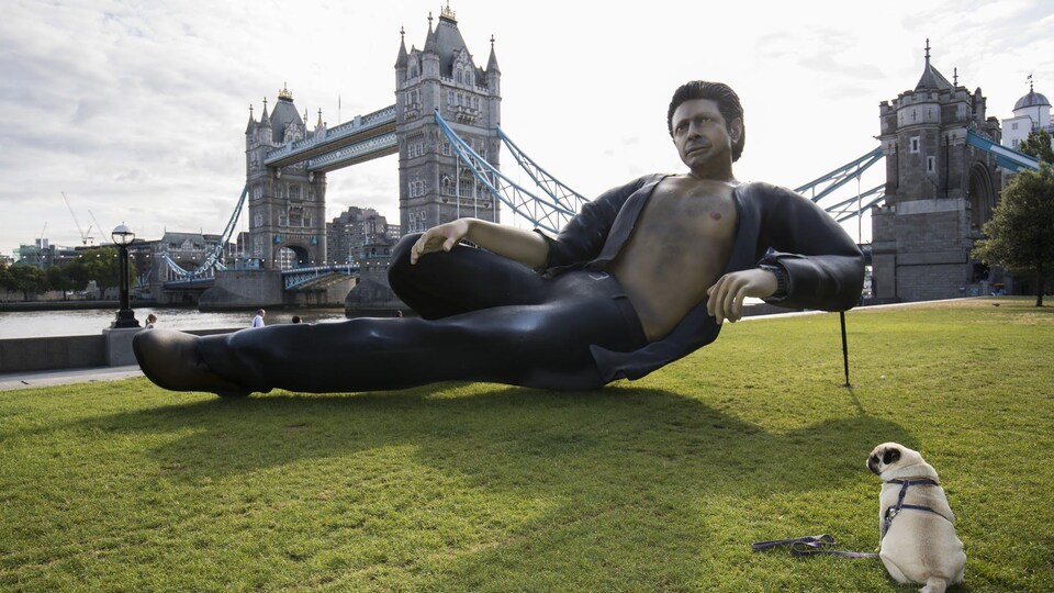 On voit la statue représentant Jeff Goldblum dans <i>Le parc jurassique</i>, avec à côté un chien et en arrière fond le Tower Bridge.