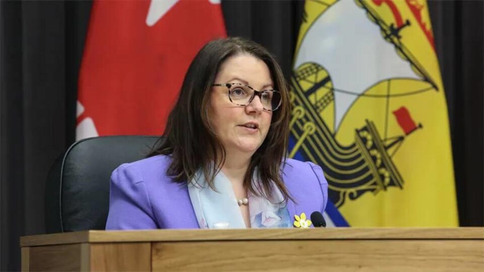Jennifer Russell assise devant un drapeau du Nouveau-Brunswick.