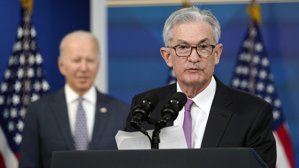 Jerome Powell prend la parole derrière un lutrin, avec Joe Biden et des drapeaux américains en arrière-plan.