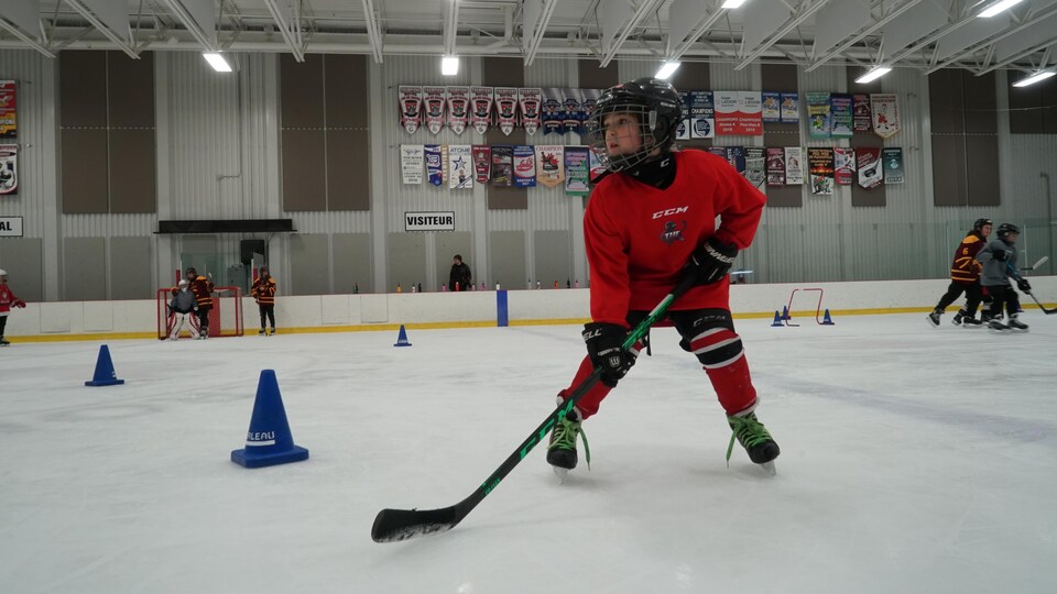 Une jeune fille habillée avec son équipement de hockey patine du reculon sur la glace.