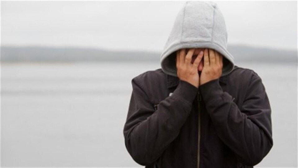 Un jeune portant un capuchon cache son visage dans ses mains