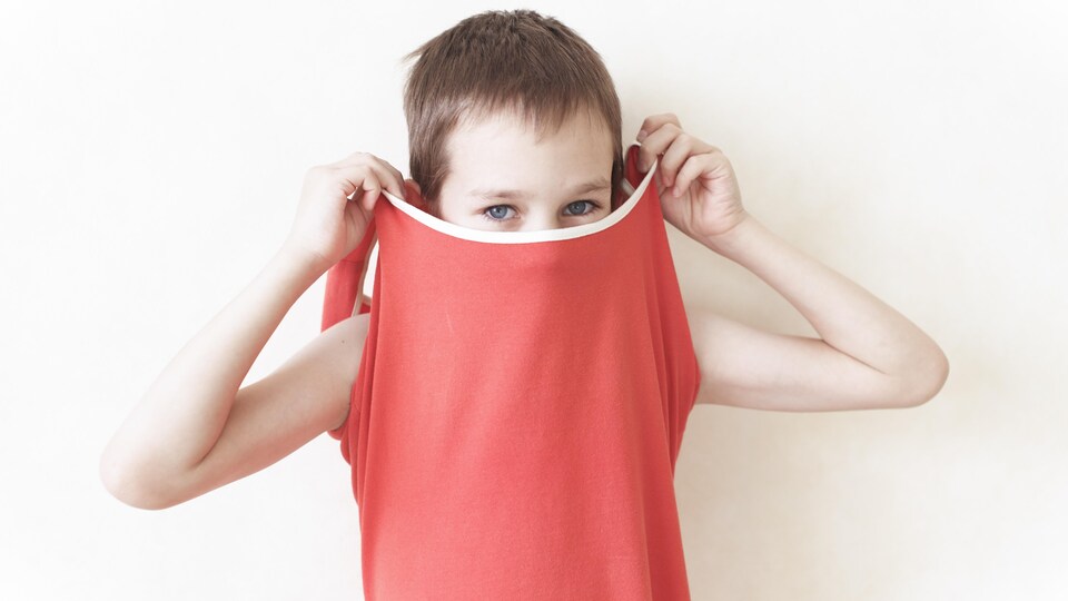 Un jeune aux cheveux courts cache son visage avec sa camisole.