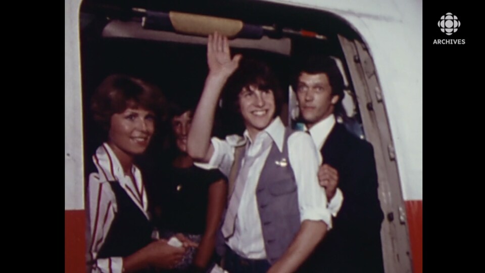 Un jeune homme salue ses proches en embarquant à bord d'un avion.