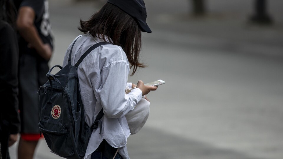 Une jeune femme regarde son cellulaire en marchant dans la rue.