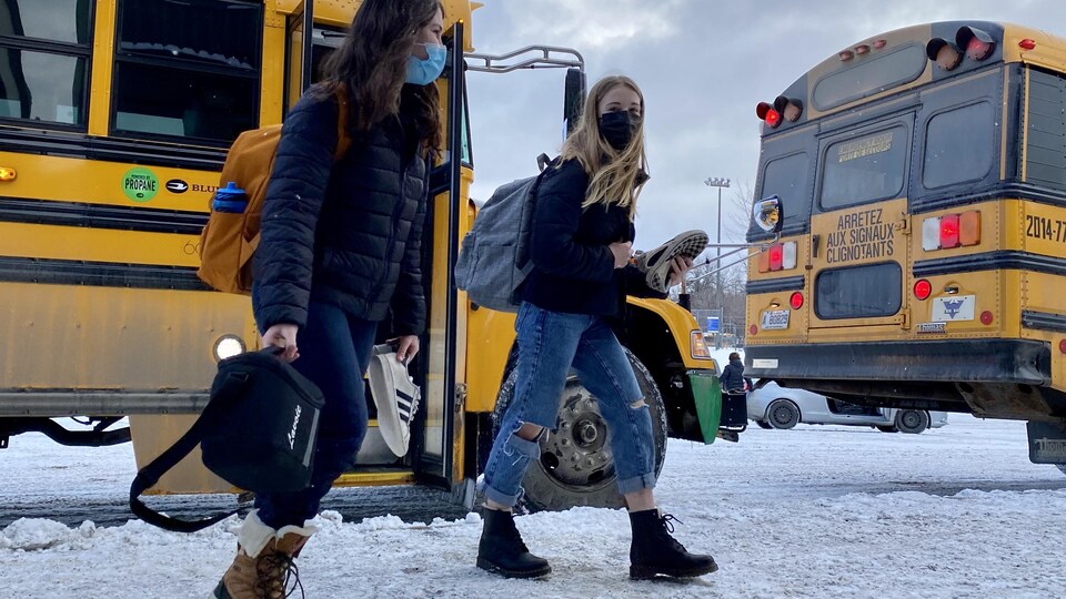 Des élèves masquées descendent de l'autobus scolaire.