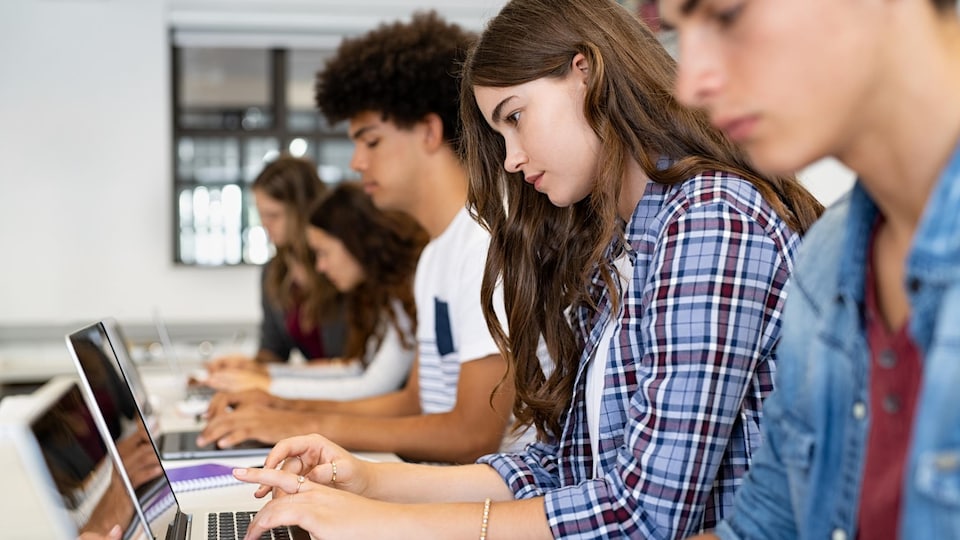 Des jeunes sont assis et assises dans une pièce devant leur ordinateur.