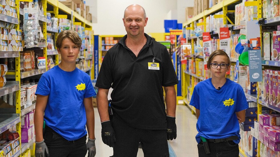 Un homme se tient avec deux jeunes employés dans une épicerie.