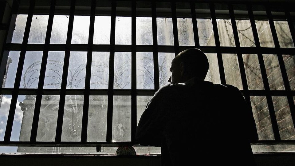 Un homme regarde à travers les barreaux de sa cellule.