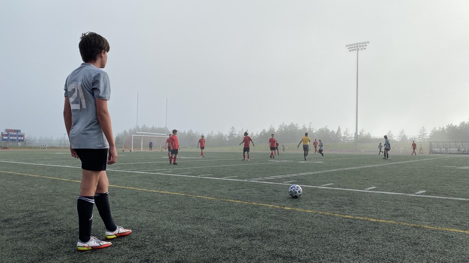 Avant de botter le ballon posé devant lui, un jeune joueur de soccer sur les lignes de côté regarde le terrain où les autres joueurs se volatilisent dans une brume épaisse.