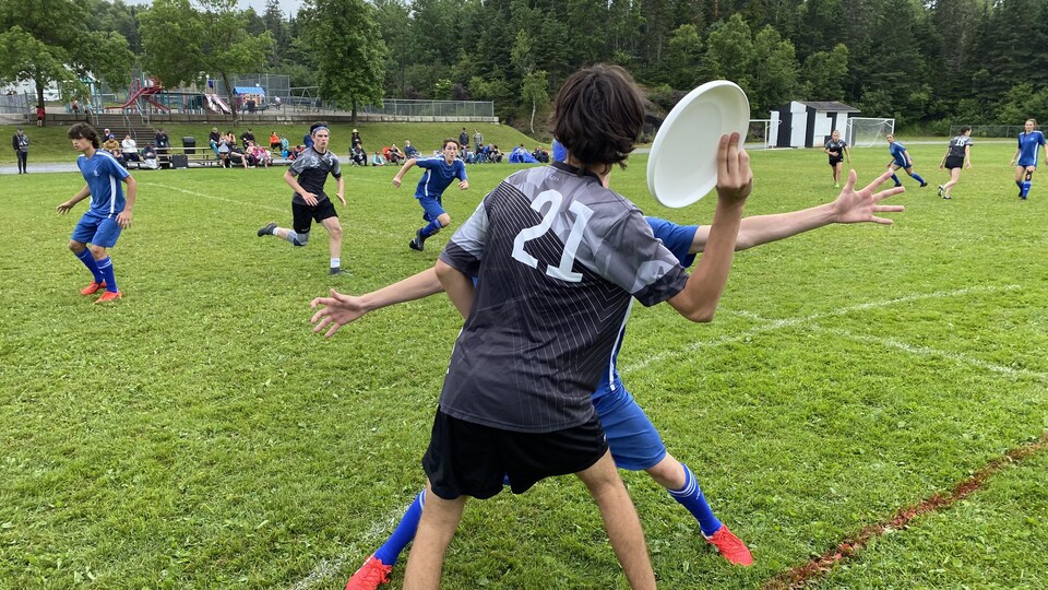 Un joueur photographié de dos se prépare à lancer le frisbee et un adversaire tente de faire un écran devant lui.