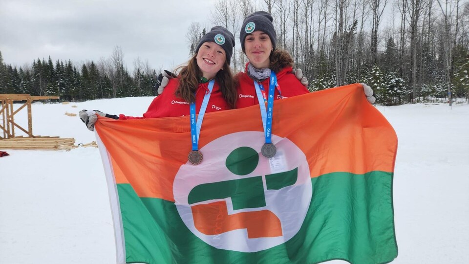 Deux jeunes athlètes, médailles au cou, exhibent le drapeau de leur région.