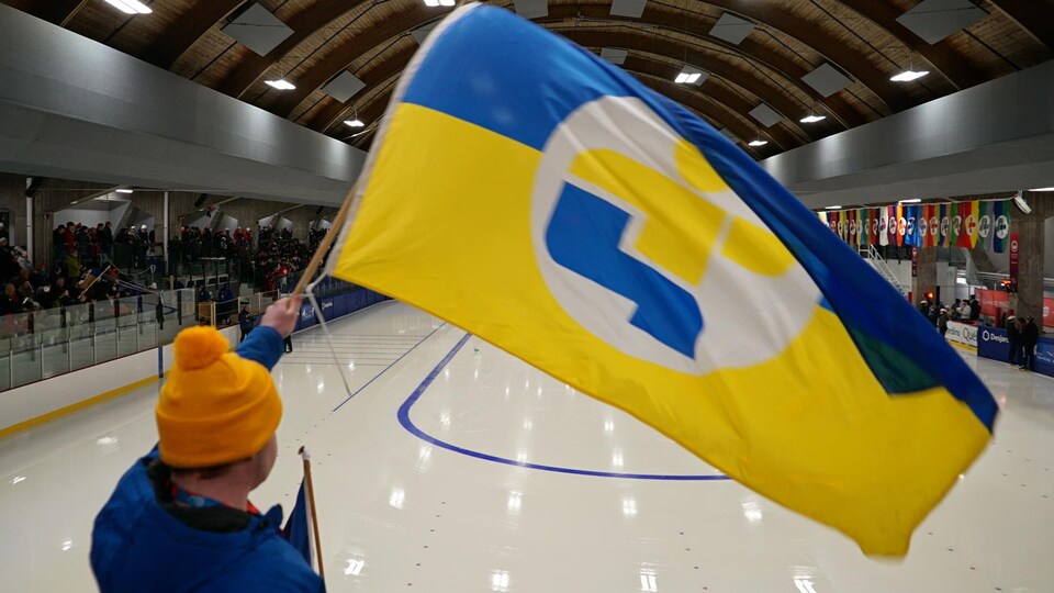 Une personne agite un drapeau géant aux couleurs de l'équipe de l'Est-du-Québec dans un aréna.