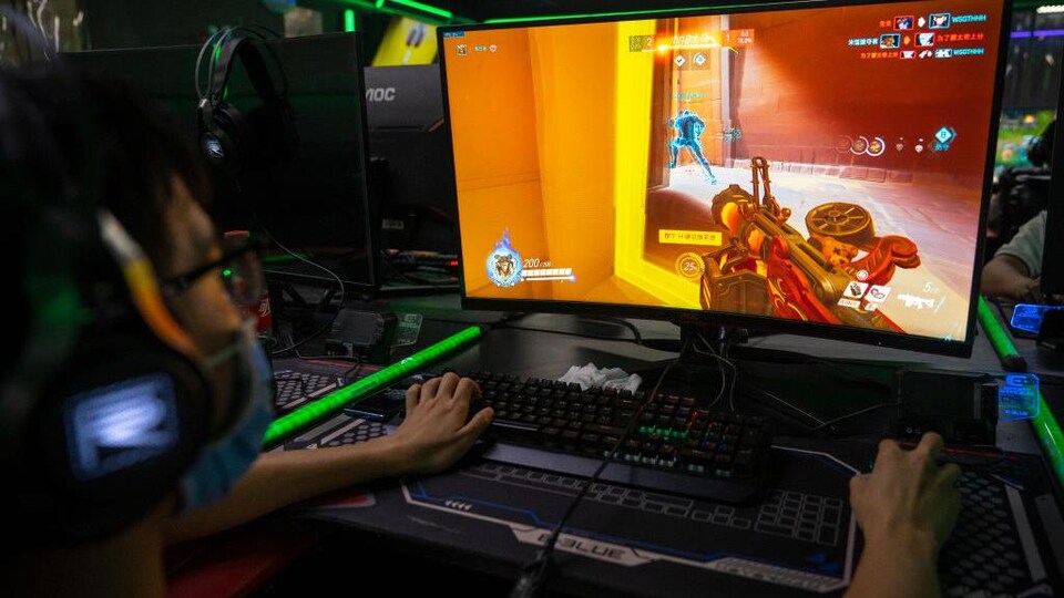 Une personne est assise devant un écran et joue à un jeu vidéo de tir à la première personne à l'aide d'un clavier et d'une souris.