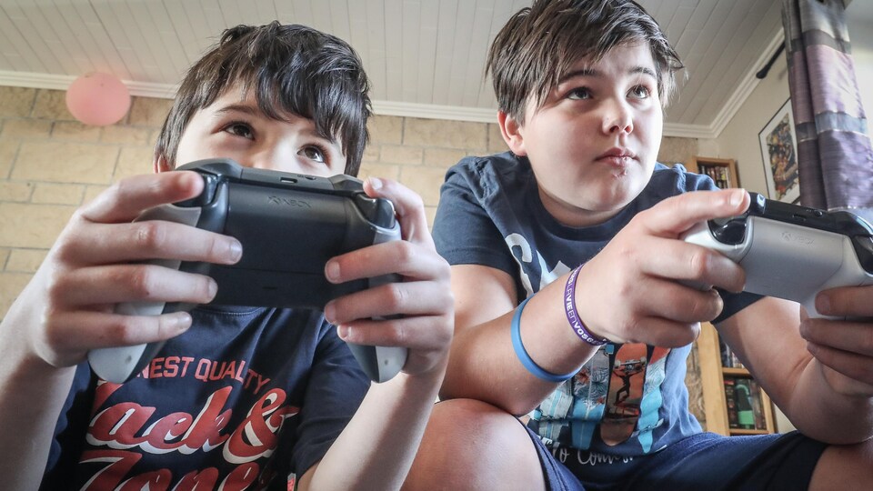 Deux jeunes garçons regardent devant eux en tenant des manettes de jeux vidéo.