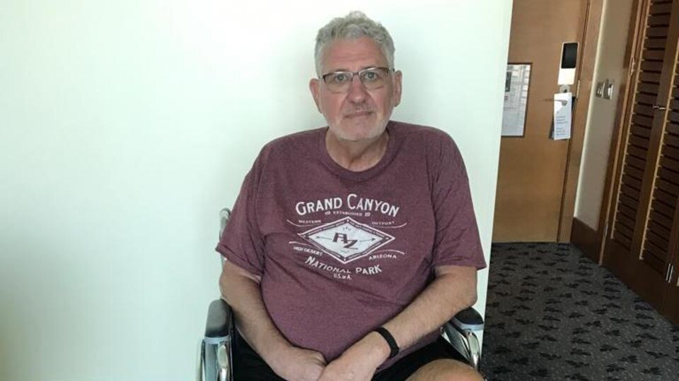 Jim Hamilton assis dans son fauteuil roulant de remplacement qui est brisé.