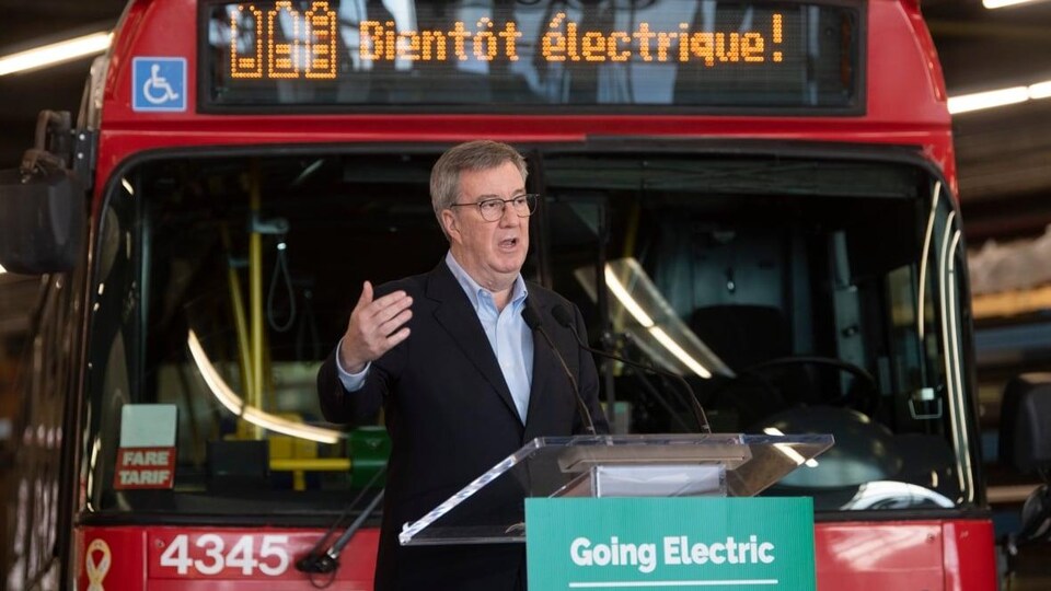 Jim Watson fait une annonce devant un autobus rouge d'OC Transpo