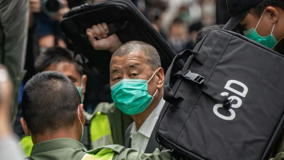 Dans la foule, un homme au crâne rasé et portant un masque regarde au loin.