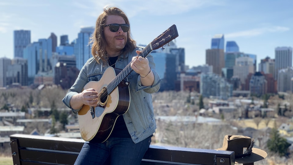 Un homme appuyé sur un banc tient joue de la guitare.