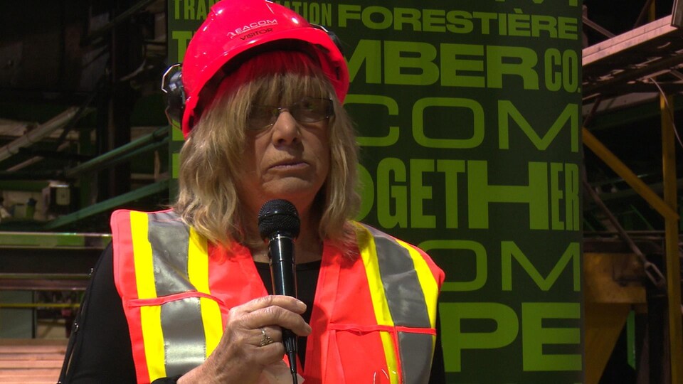 Joanne raconte son histoire devant une cinquantaine de travailleurs. Elle porte un casque de sécurité sur la tête.