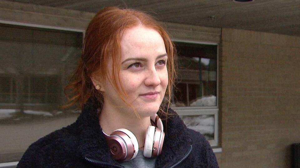 Joannie Levesque debout à l'extérieur devant un bâtiment. Elle a des écouteurs roses autour du cou.
