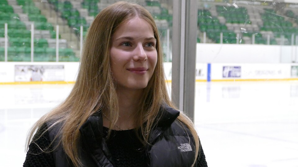 Une jeune femme accorde une entrevue aux abords d'une patinoire intérieure.