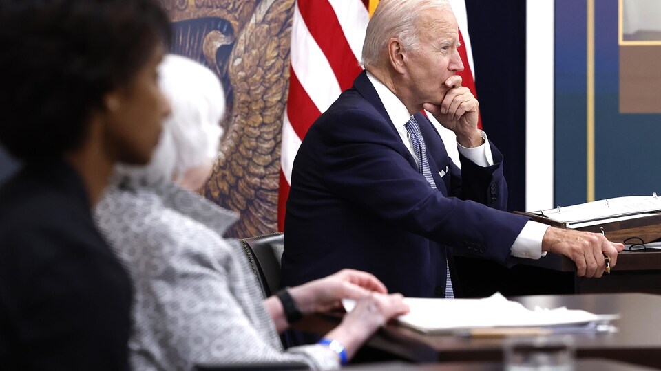 Le président américain Joe Biden, la main sur la bouche, écoute lors d'une réunion.