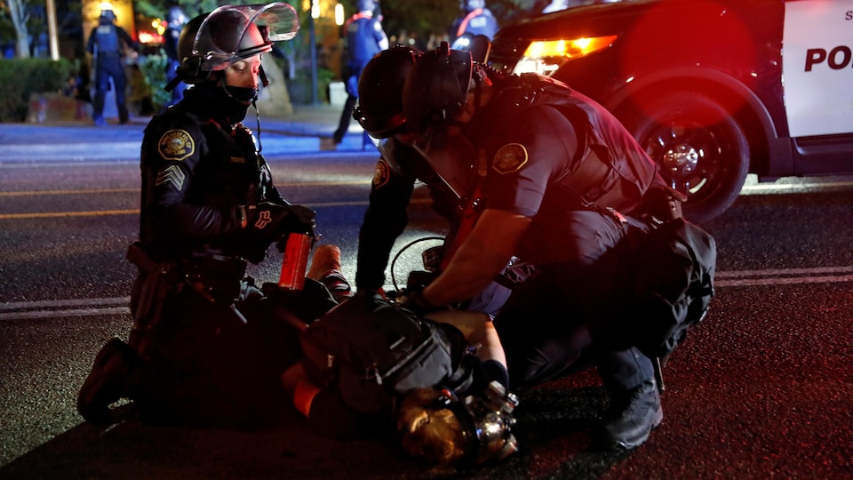 Trois policiers arrêtent un manifestant lors d'une manifestation contre la violence policière et l'injustice raciale.