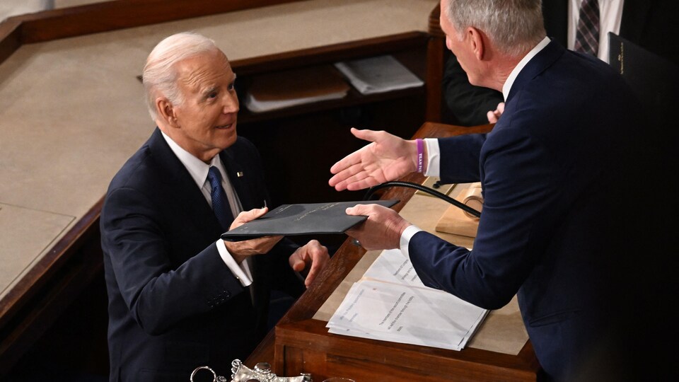 Le président Joe Biden remettant un document à un homme vu de dos.