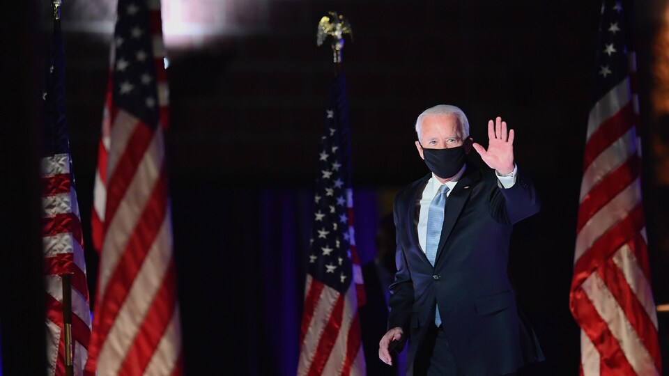 Joe Biden arrive sur scène masqué pour donner son discours. Il salue la foule.