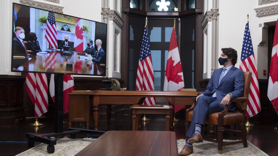 Justin Trudeau regarde un écran de télévision dans lequel apparaît Joe Biden.