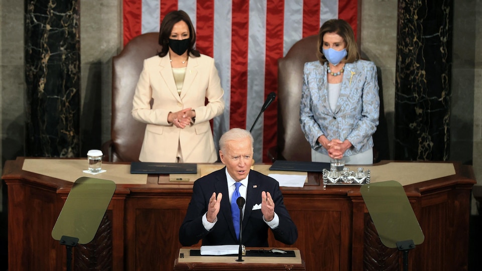 Joe Biden prononce un discours. Kamala Harris et Nancy Pelosi l'écoutent attentivement à l'arrière.