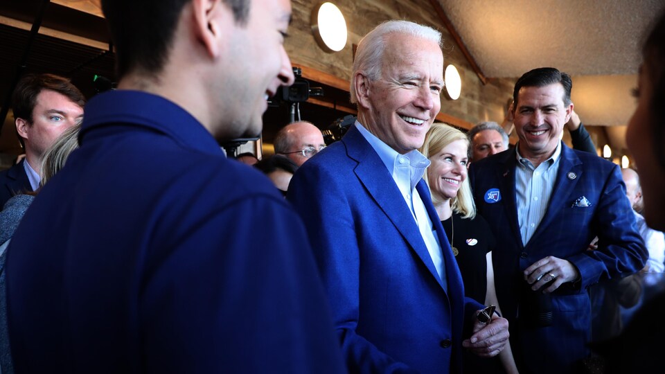 Entouré de deux hommes, Joe Biden serre la main d'une femme, le sourire aux lèvres.