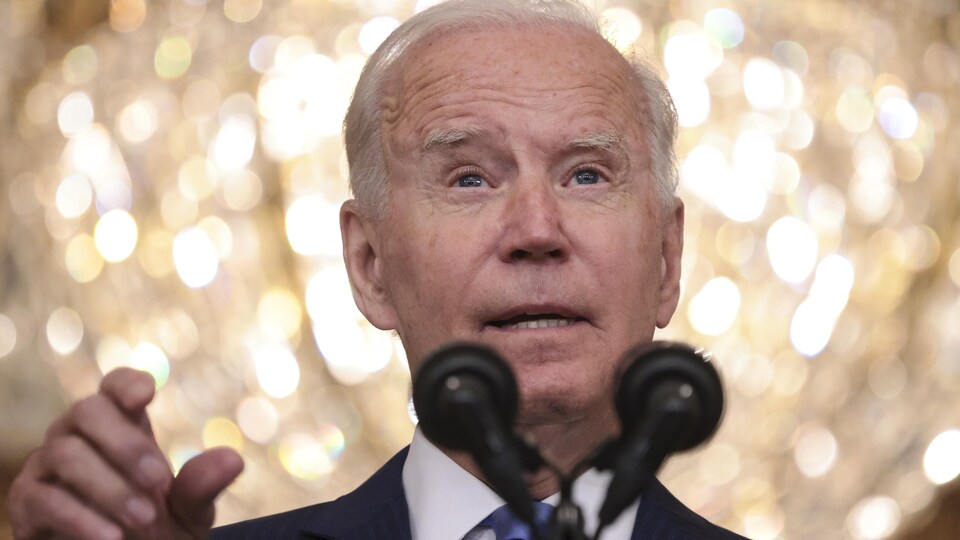 Joe Biden parle dans un micro, devant une boule lumineuse.