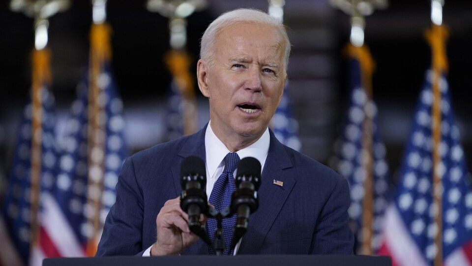 Joe Biden parle au micro devant des drapeaux américains.