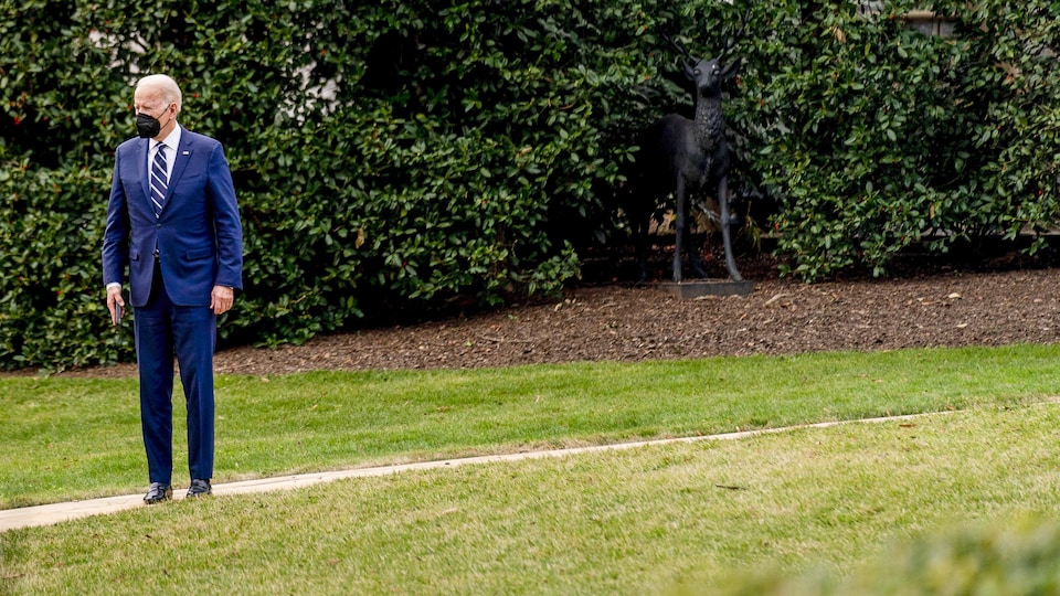 Le président Joe Biden portant un couvre-visage est debout et seul dans le jardin de la Maison-Blanche.