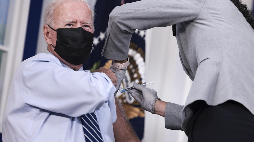 Joe Biden, masqué, reçoit une piqûre dans le bras gauche.