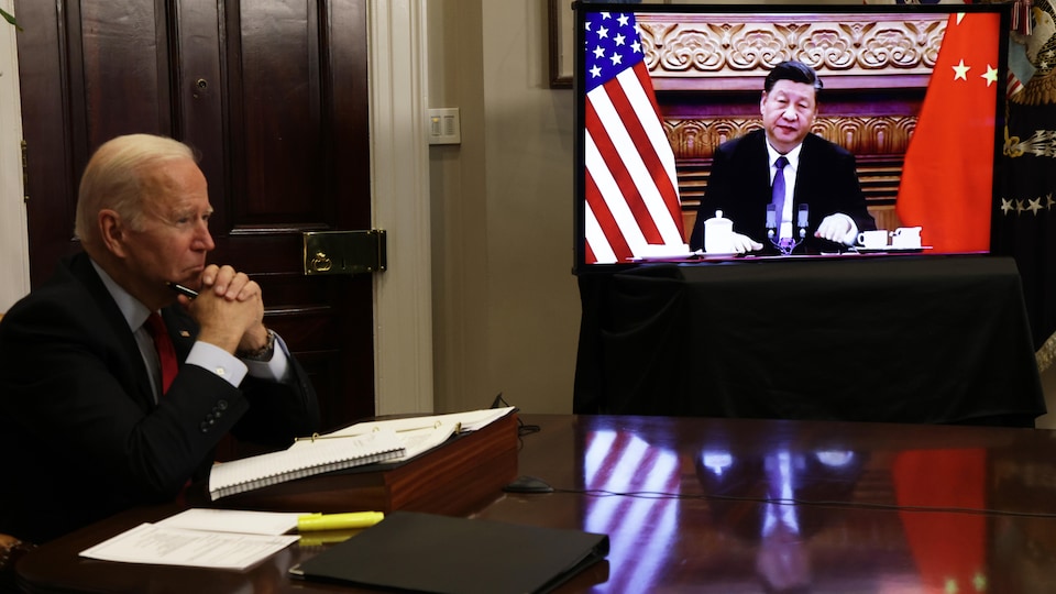 Joe Biden est assis à côté d'un écran où apparaît le président chinois Xi Jinping.