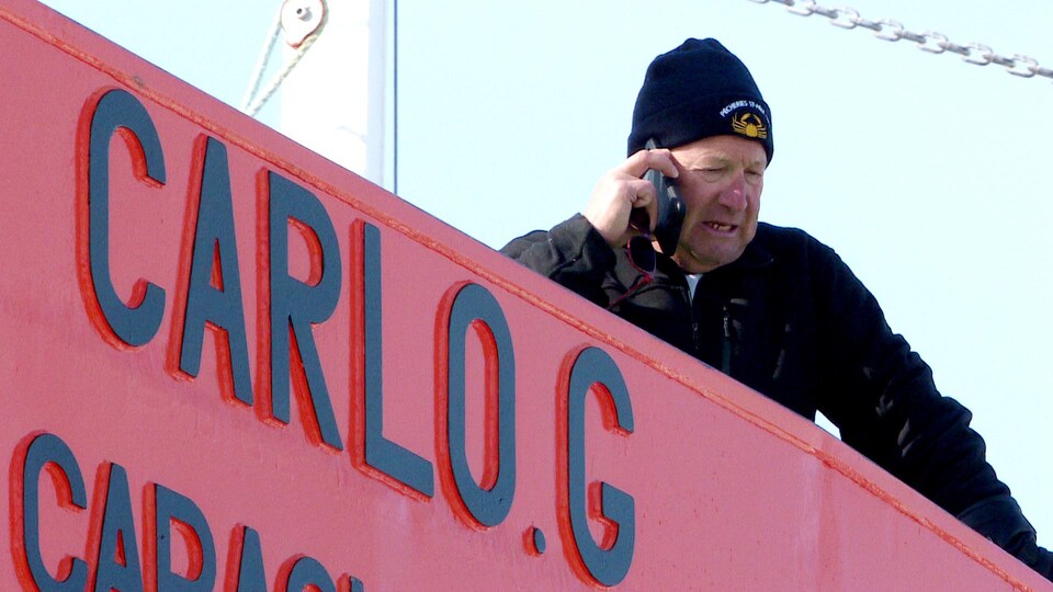 Un pêcheur parle au téléphone, sur son bateau.