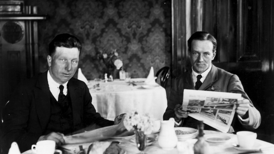 John Alcock et Arthur Brown à table avec des journaux et un repas.