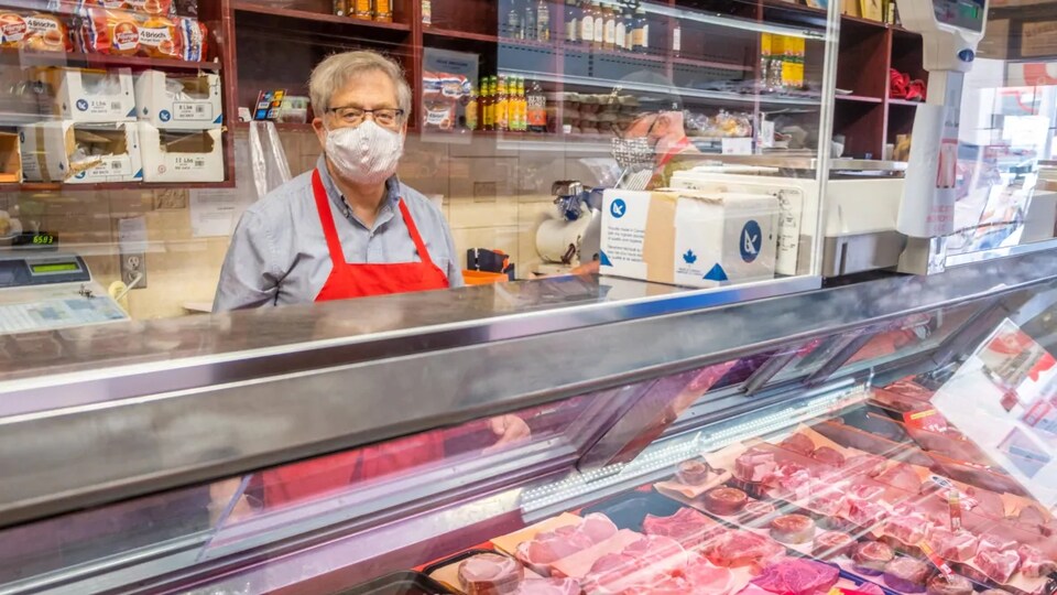 John Diener pose pour la caméra derrière un comptoir de viandes.