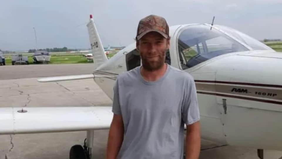 John Fehr avec un chandail gris près d'un avion.