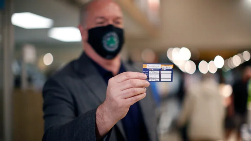John Horgan montrant une carte indiquant qu'il a été vacciné contre la COVID-19.