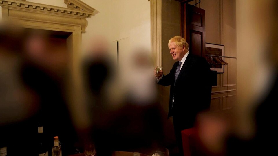 Boris Johnson, souriant, tient un verre dans sa main droite. 