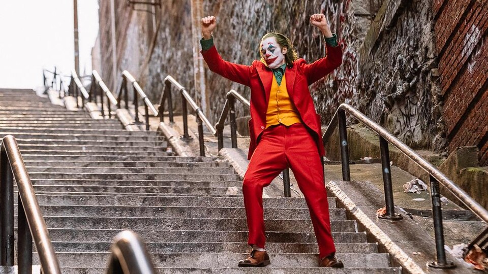 Un homme déguisé en clown est debout dans un escalier, les bras en l'air.