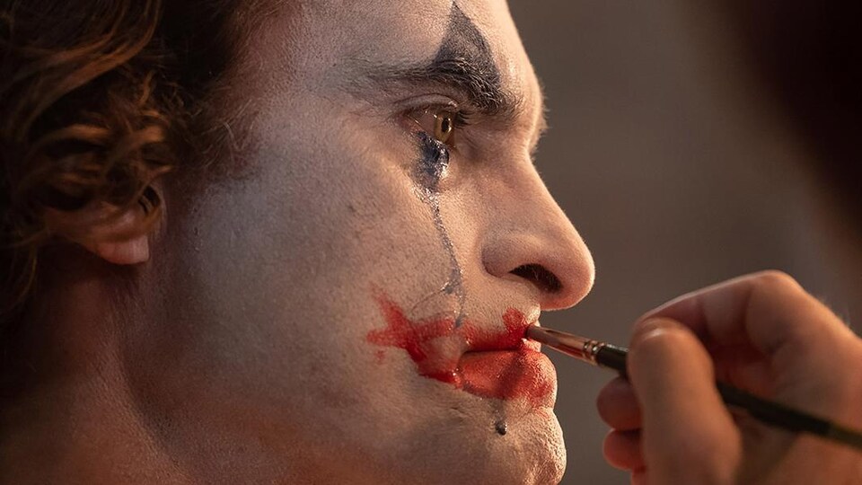 Un homme applique du maquillage de clown sur son visage.