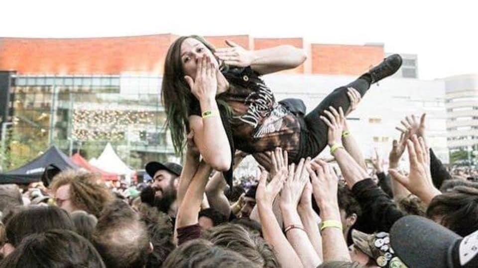 Une femme est transportée par plusieurs personnes qui la tiennent au bout de leurs bras dans un concert extérieur.
